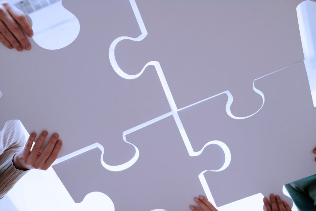 Varias personas encajan piezas de un puzzle azul claro, como metáfora de la unificación de información.